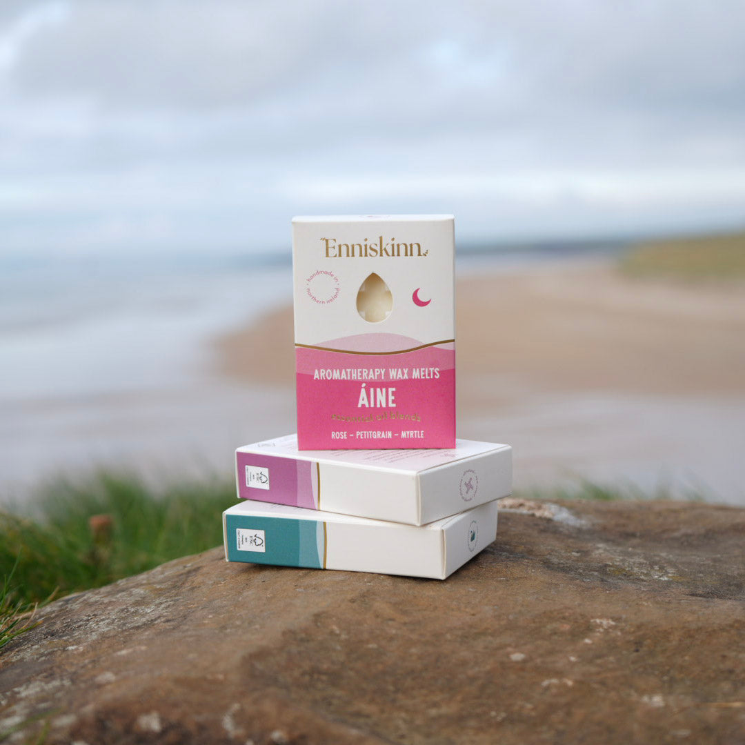 Aine Aromatherapy Wax Melts display stacked on a rock by the sea with pink packaging on top