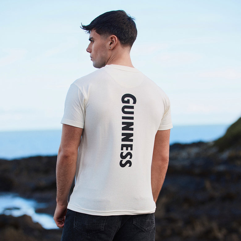 Back view of a man in a white Guinness T shirt with GUINNESS printed vertically down the back.