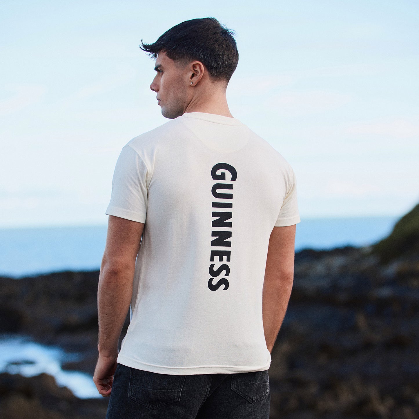 Back view of a man in a white Guinness T shirt with GUINNESS printed vertically down the back.