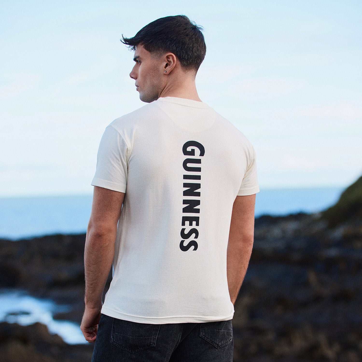 Back view of a man in a white Guinness T shirt with GUINNESS printed vertically down the back.
