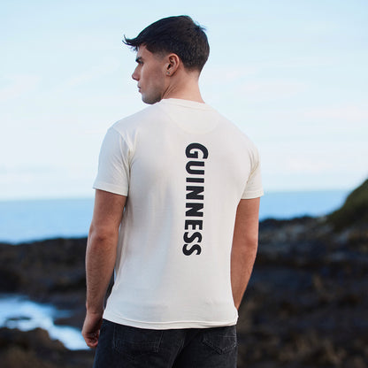 Back view of a man in a white Guinness T shirt with GUINNESS printed vertically down the back.