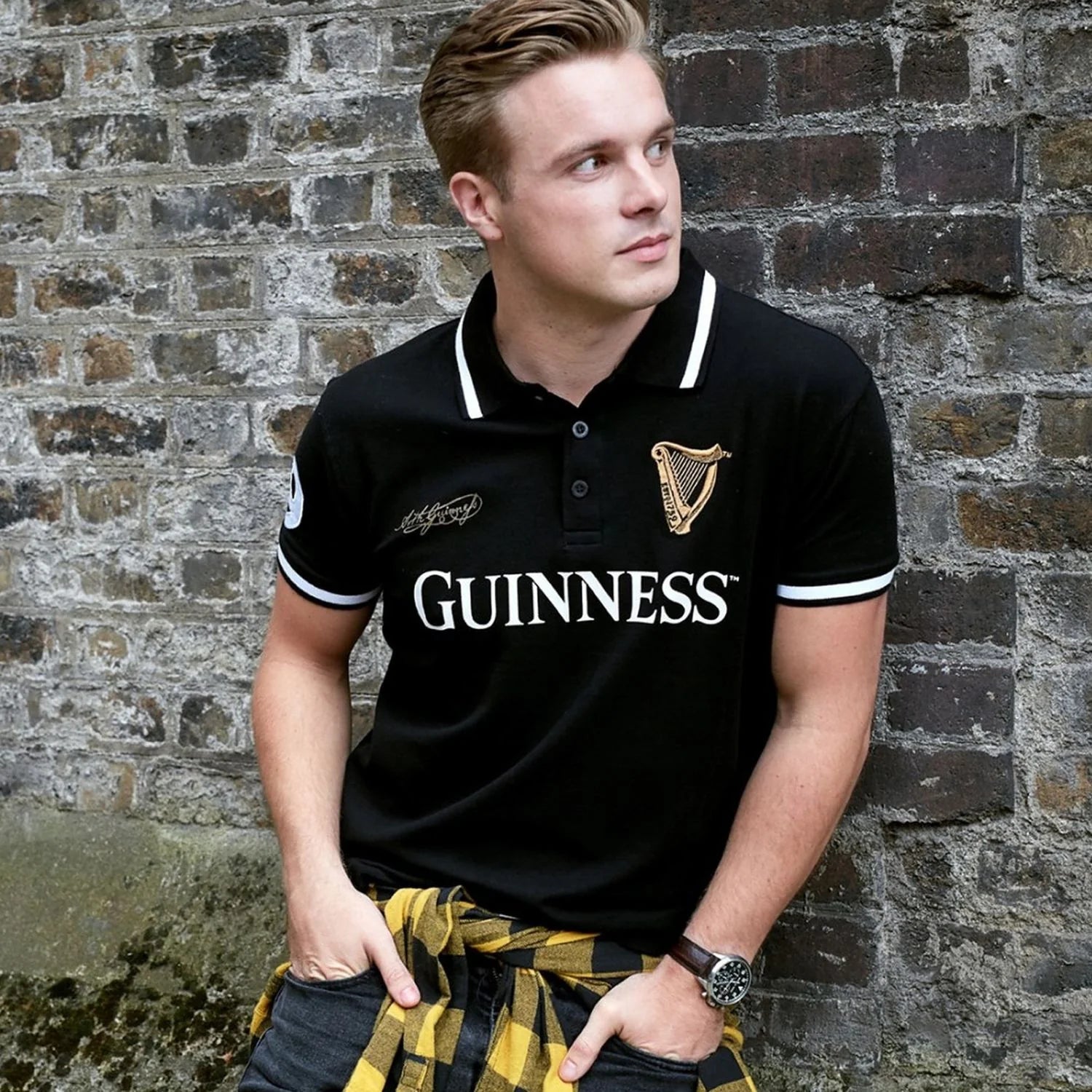 Man wearing a black Guinness polo with white trim posing against a brick wall