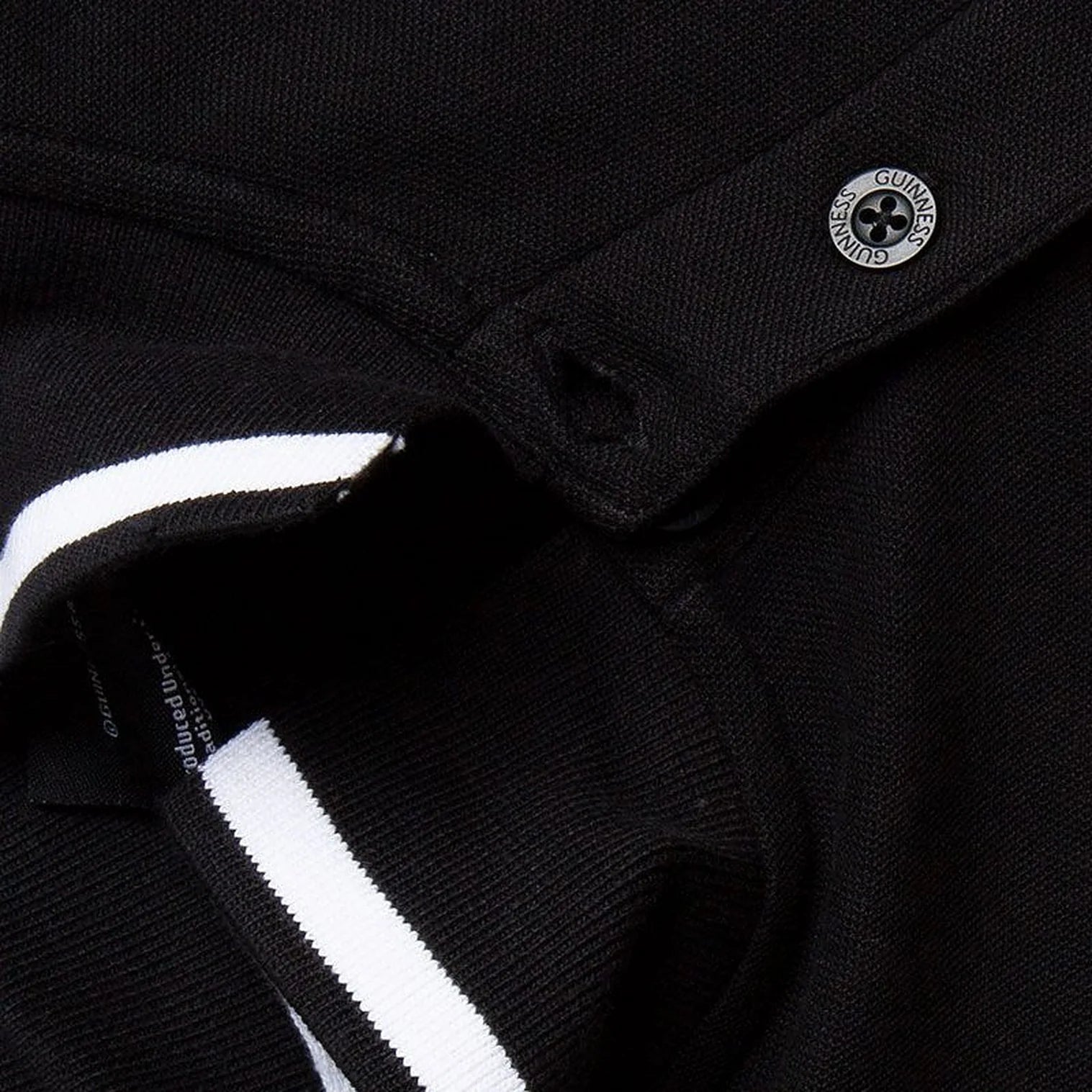 Close up of black polo collar with white stripe and a circular Guinness badge