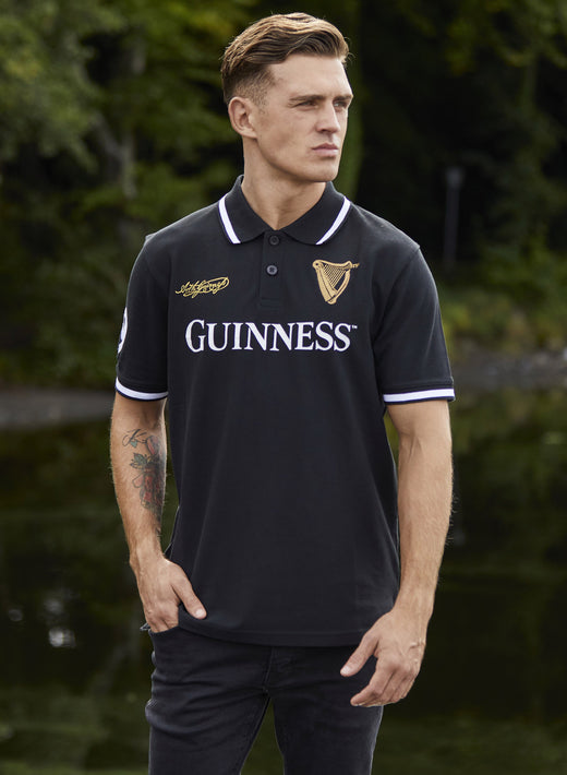 Man wearing black Guinness polo shirt standing outdoors near water