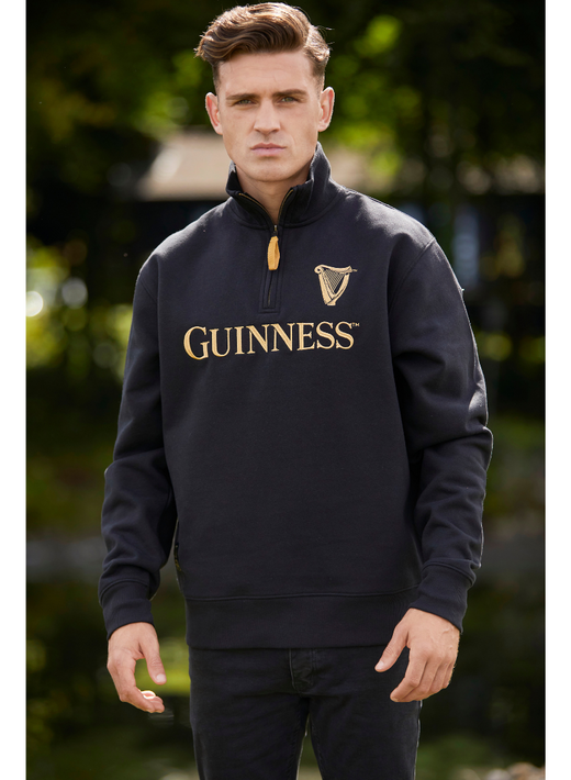 Man wearing black Guinness sweatshirt standing outdoors with serious expression