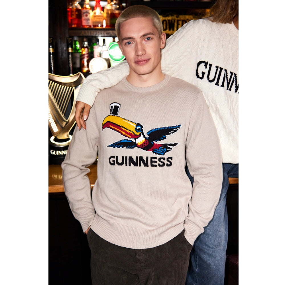 Model wearing beige Guinness Flying Toucan crew neck jumper with a bold bird motif