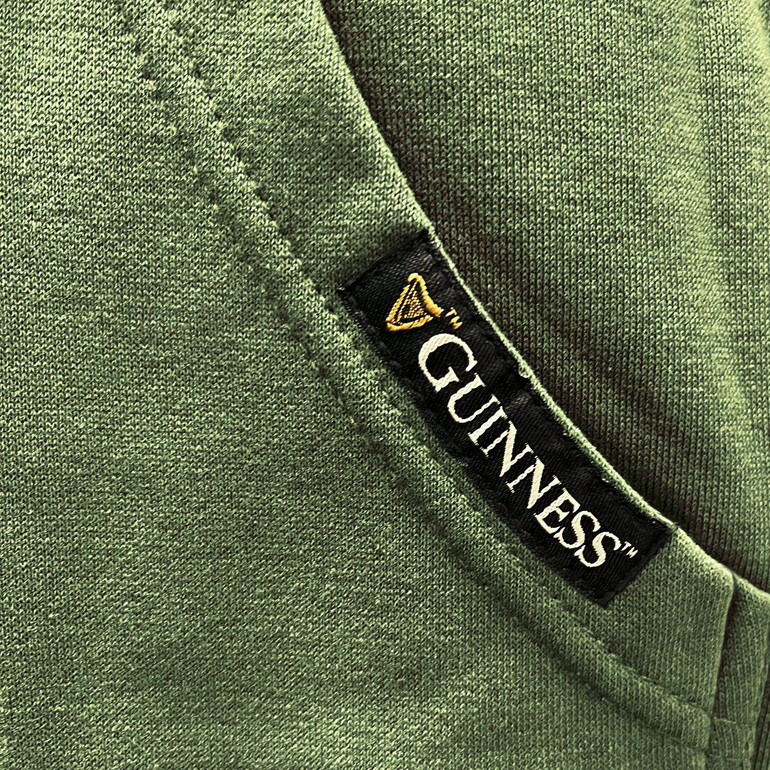 Black Guinness label tag sewn onto a green hoodie near the pocket