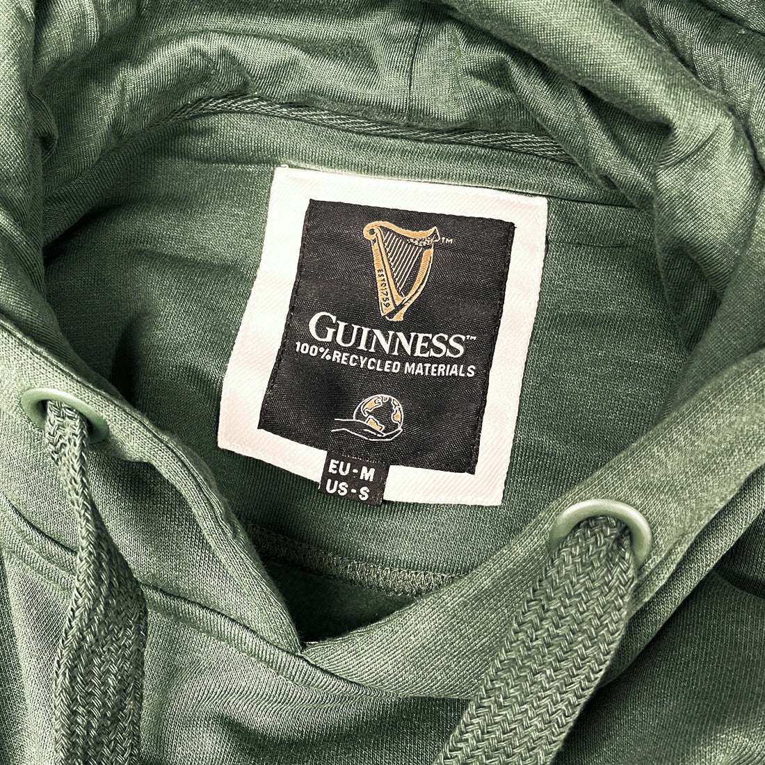 Guinness bottle green hoodie interior label featuring 100% recycled materials and size tag