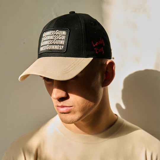 Man wearing black and beige cap with text patches in sunlight