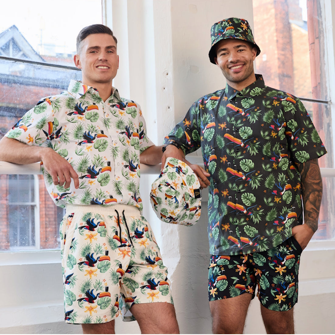Two men wearing matching tropical print shirts and shorts indoors