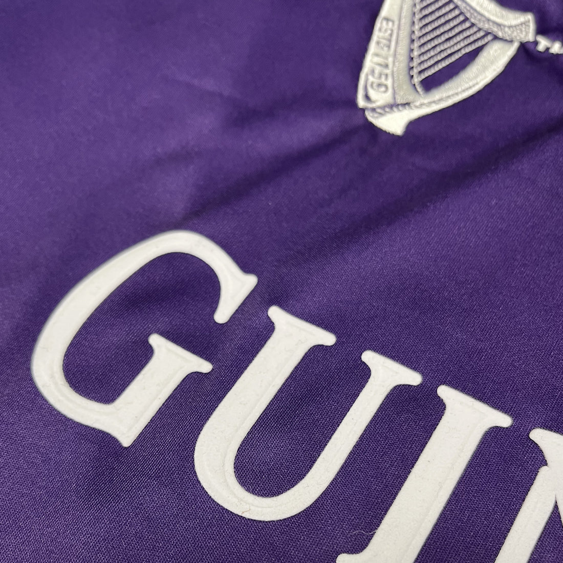 Close-up of purple fabric with white GUINNESS lettering and crest on the jersey.