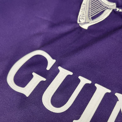 Close-up of purple fabric with white GUINNESS lettering and crest on the jersey.