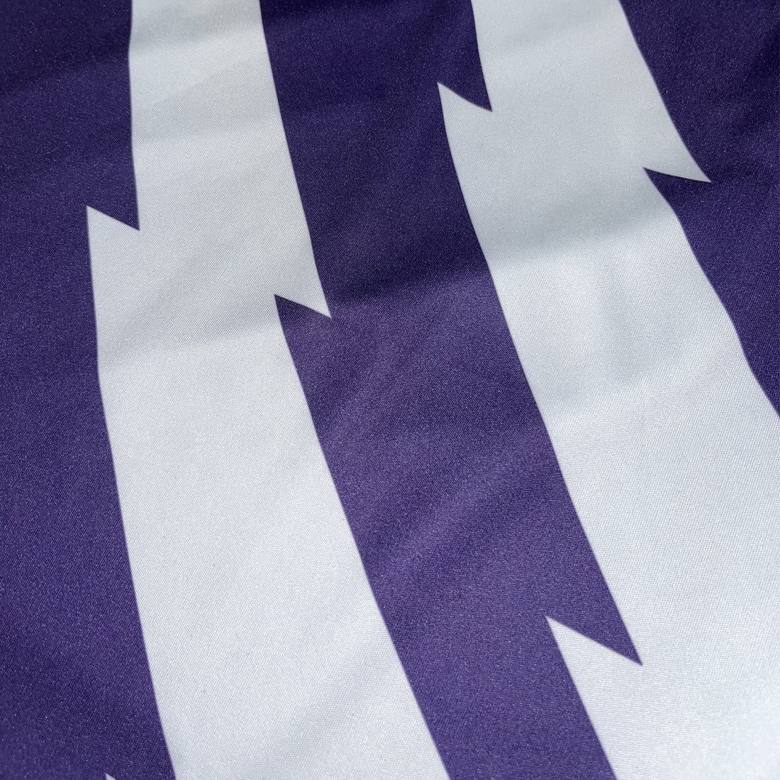 Close-up of purple fabric with large white angular stripes from a Guinness Premier League football top.