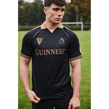 Guinness black football top with copper trim and gold lettering worn by a male model on a grassy field