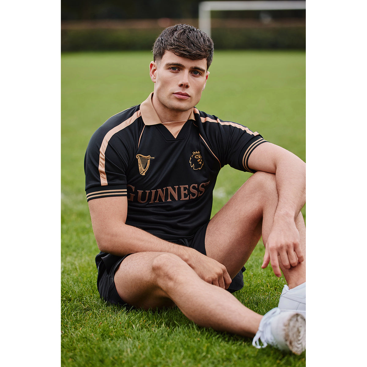 Man wearing the black Guinness Premier League football top with copper trim on a grassy field