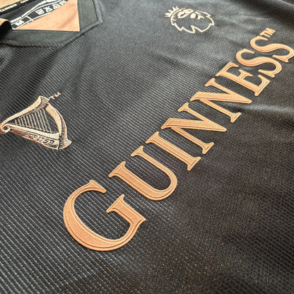 Close-up of black Guinness football top fabric with copper lettering and crest