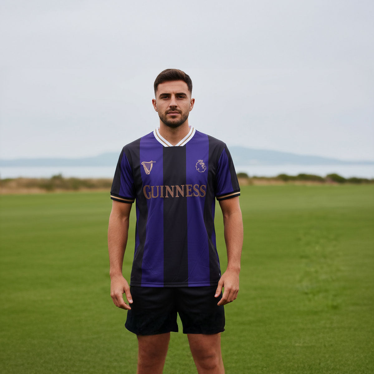 Man wearing purple and black Guinness football top standing on a grassy field.
