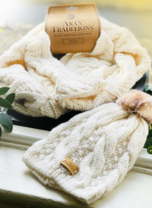 Cream-colored knitted hat with pom-pom and matching scarf on windowsill