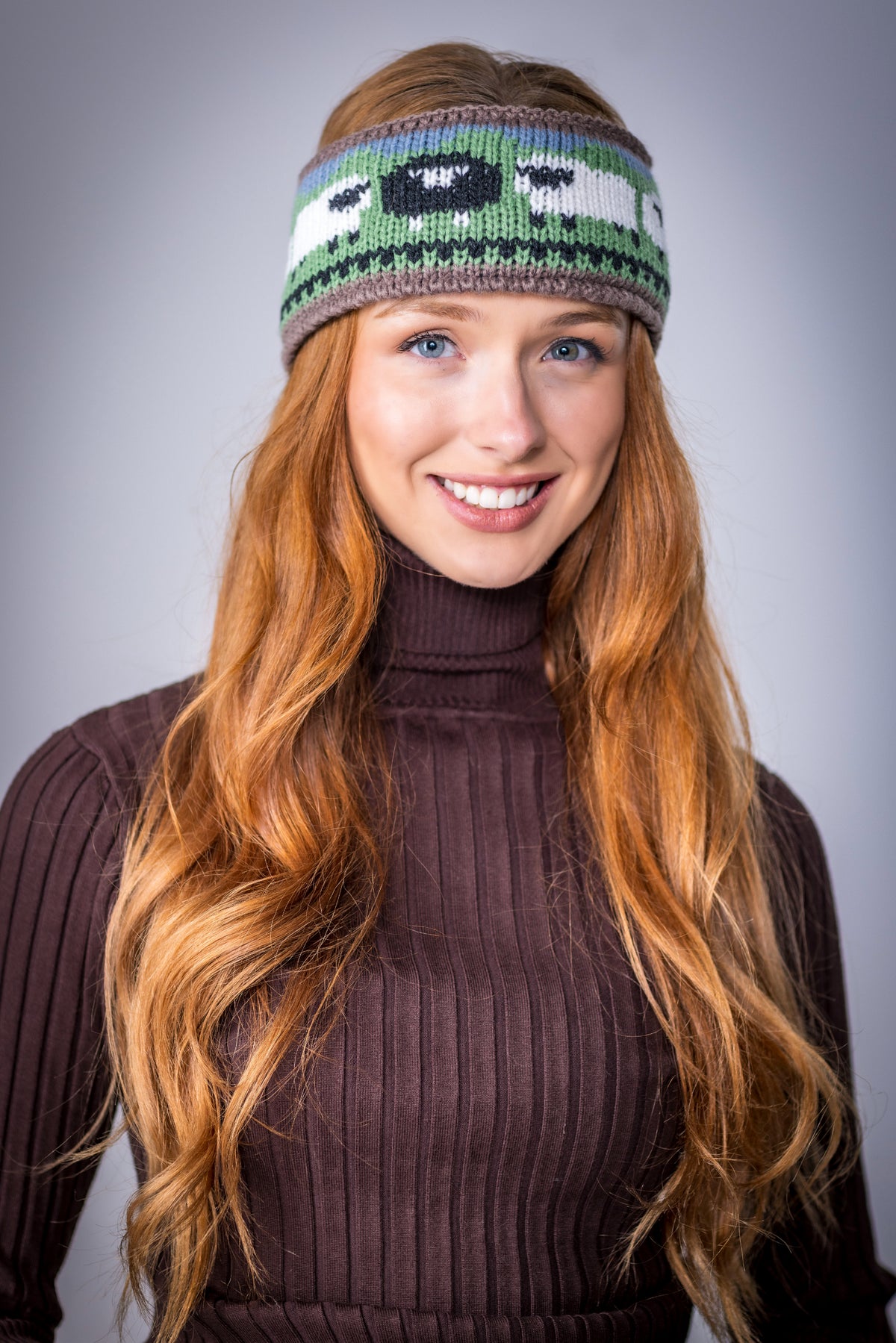 Smiling woman with long red hair wearing a knitted headband and brown turtleneck