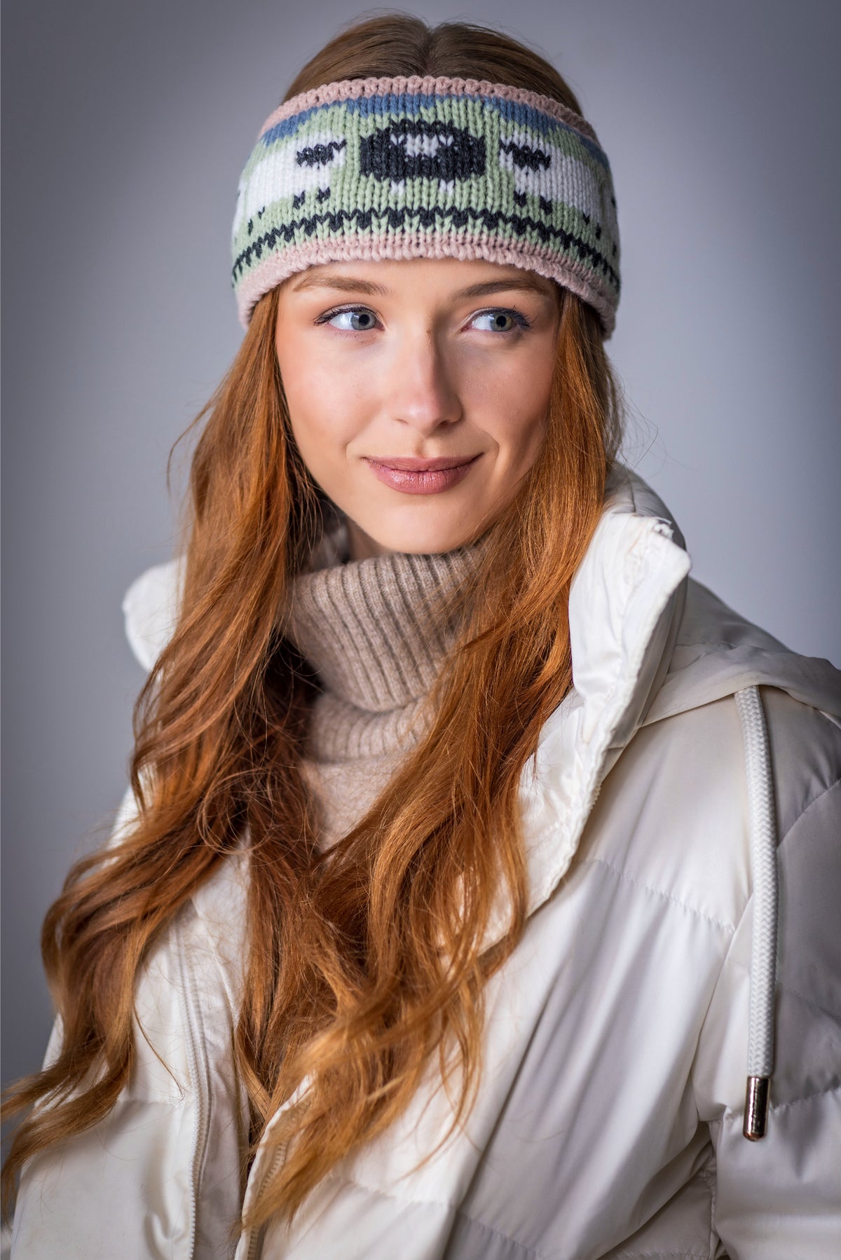 Young woman with long red hair wearing knitted headband and white winter jacket