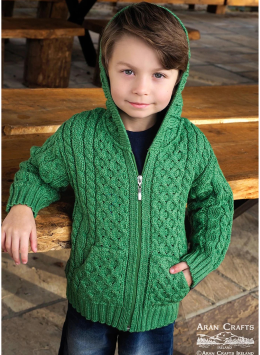 Young boy wearing a green knitted hooded sweater standing by wooden table