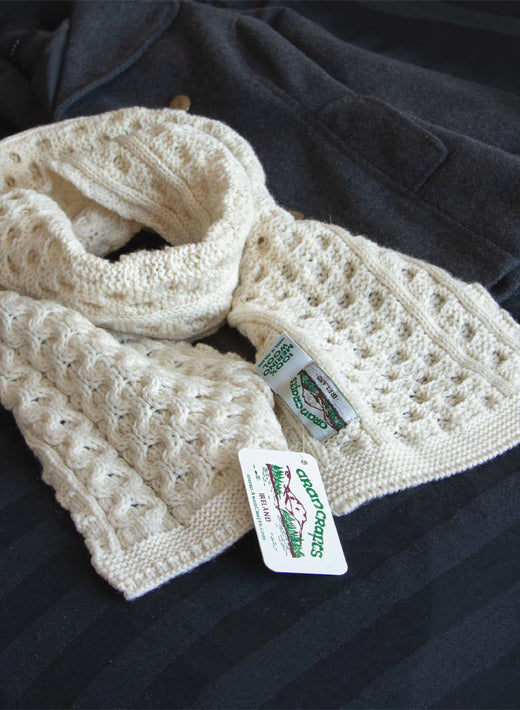 Cream-colored knitted wool scarf with textured patterns and tags attached