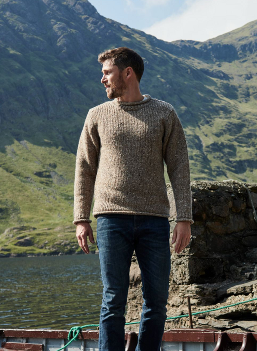 Man wearing sweater standing near lake with mountains in background