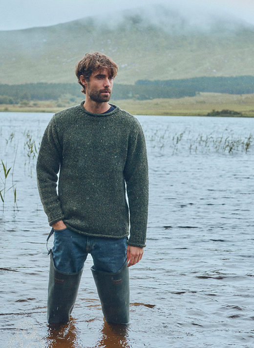 Man wearing green sweater and waders standing in shallow lake water