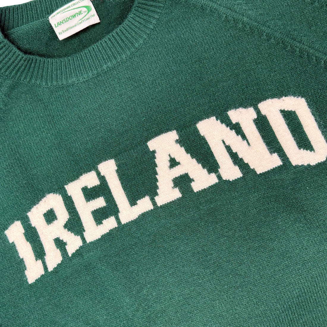 Close-up of green knitted jumper fabric showing large white IRELAND lettering and a clothing tag