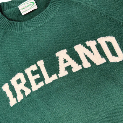 Close-up of green knitted jumper fabric showing large white IRELAND lettering and a clothing tag