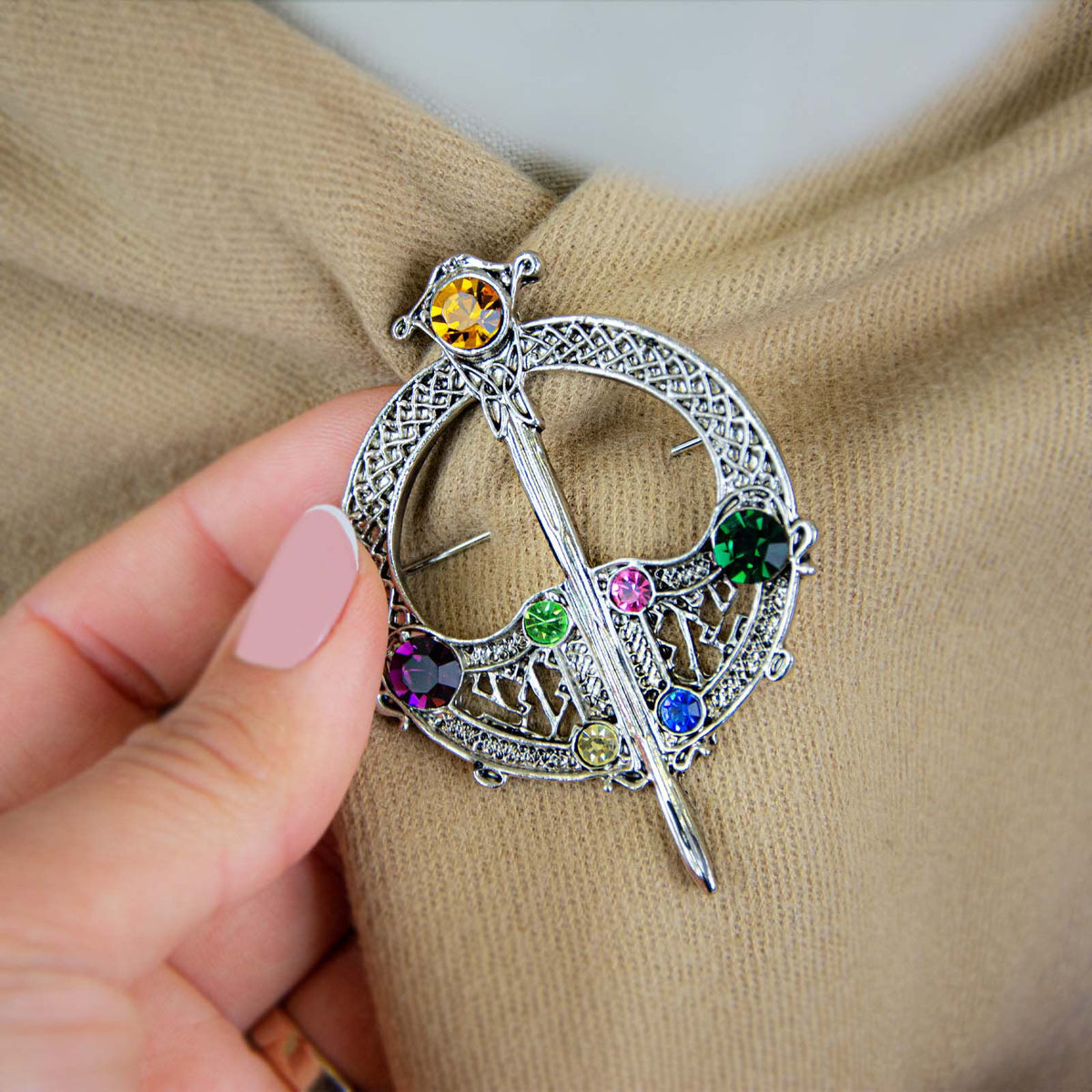 Hand holding silver brooch with colorful gemstones on beige fabric