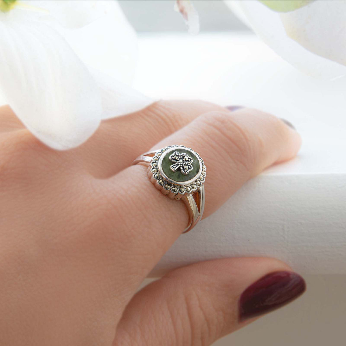 Hand wearing silver ring with green stone and clover design