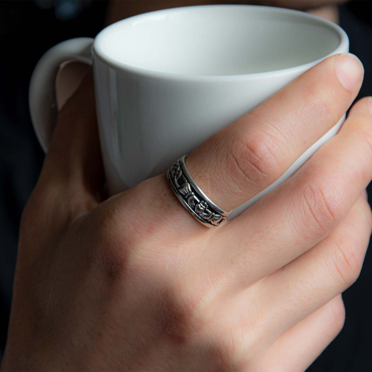 Hand wearing a decorative silver ring holding a white ceramic cup