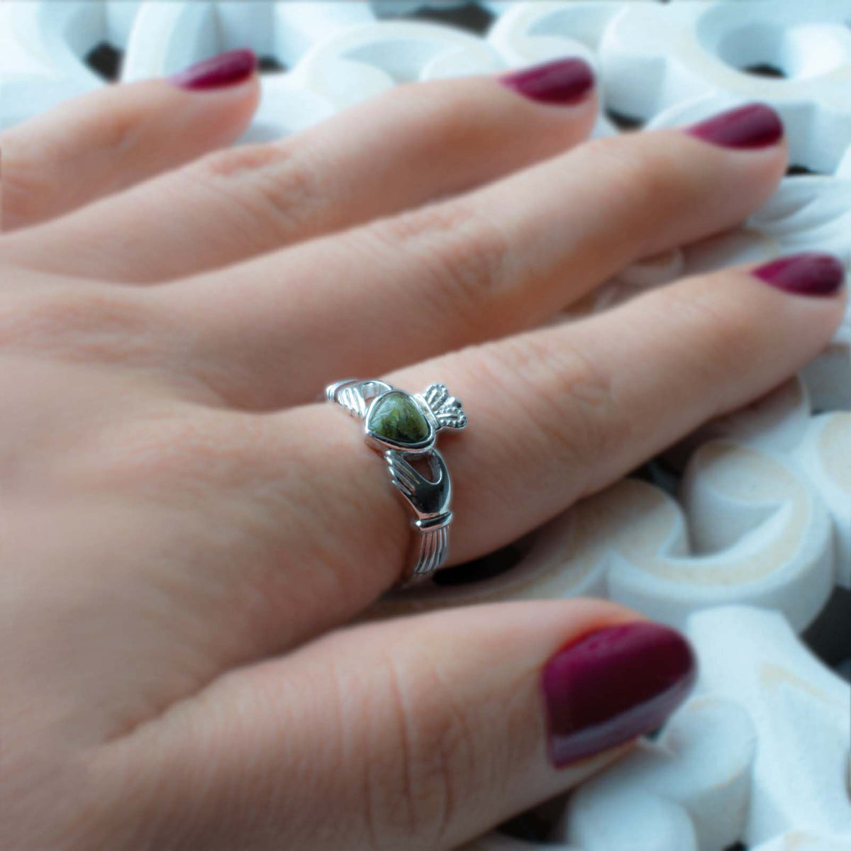 Hand with dark red nail polish wearing a silver ring with green stone