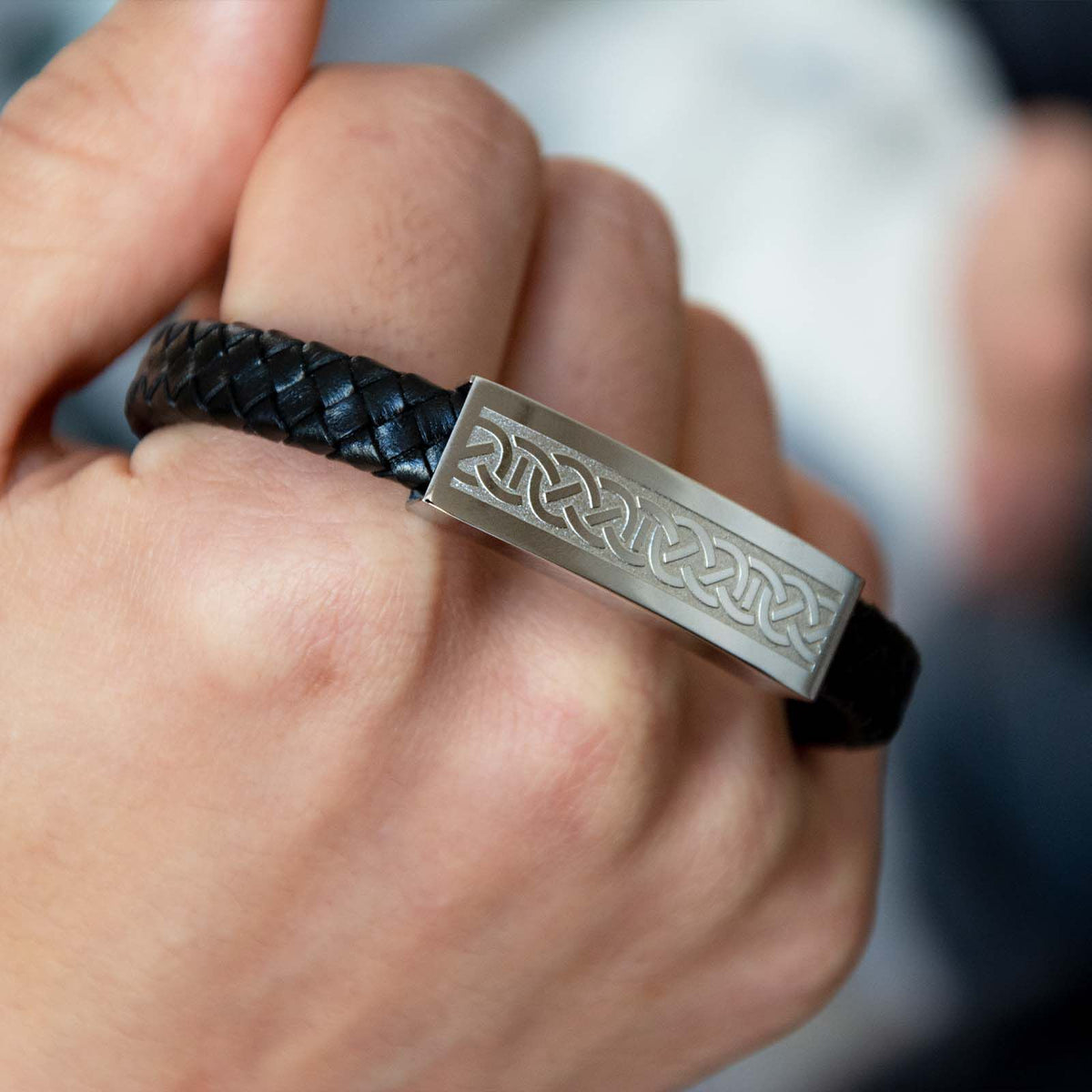 Hand holding black braided leather bracelet with engraved metal plate