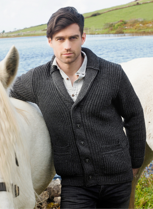 Man wearing dark knit cardigan standing beside white horse near water