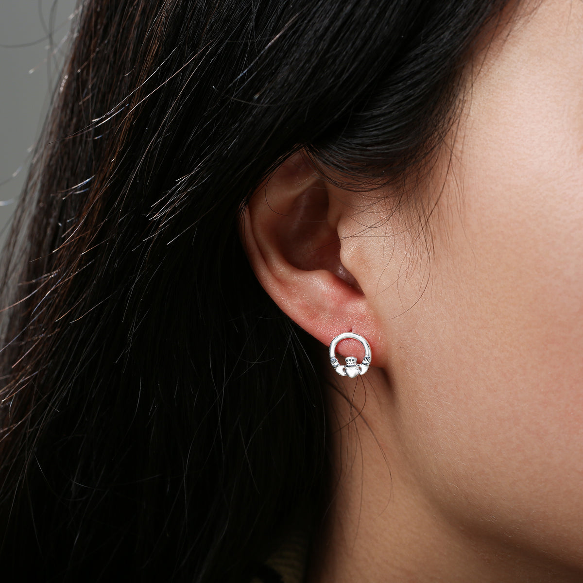 Close-up of ear wearing a silver circular stud earring with heart detail