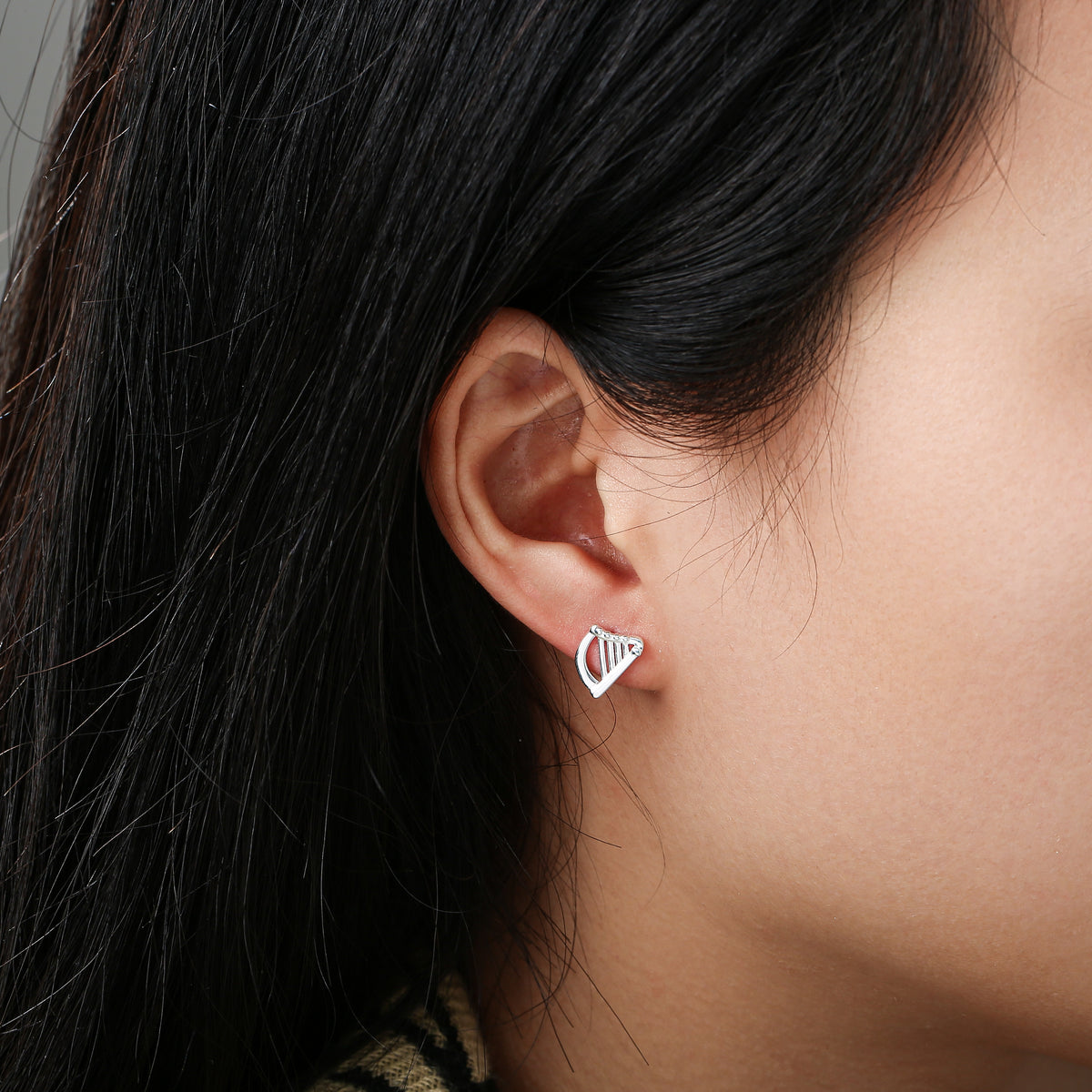 Close-up of ear wearing a small silver harp-shaped stud earring