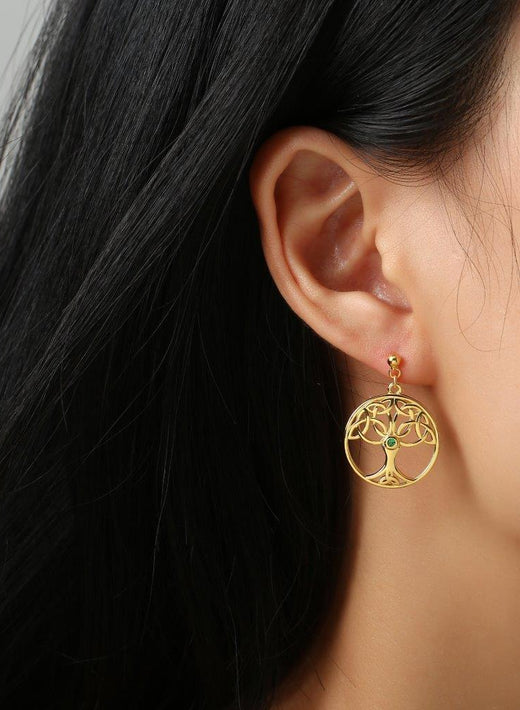 Close-up of ear wearing gold tree of life dangle earring with green stone