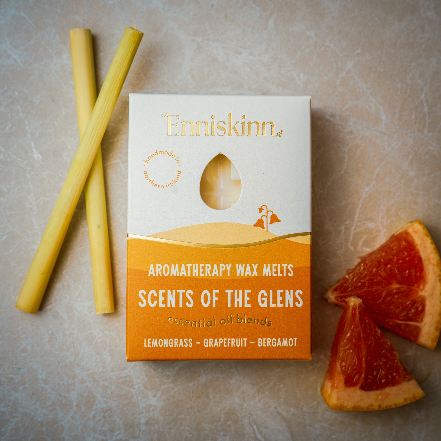 Enniskinn Aromatherapy Wax Melts Scents of the Glens box on a textured surface with lemongrass sticks and grapefruit wedges.