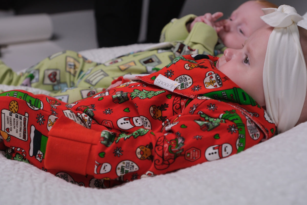 Two babies lying down wearing colorful holiday-themed pajamas