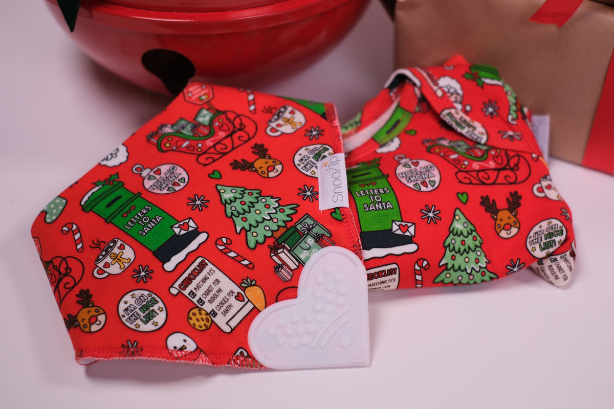 Two red Christmas-themed baby bibs with festive illustrations and a white heart teether