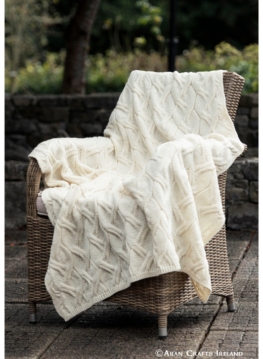Cream cable knit blanket draped over a wicker chair outdoors
