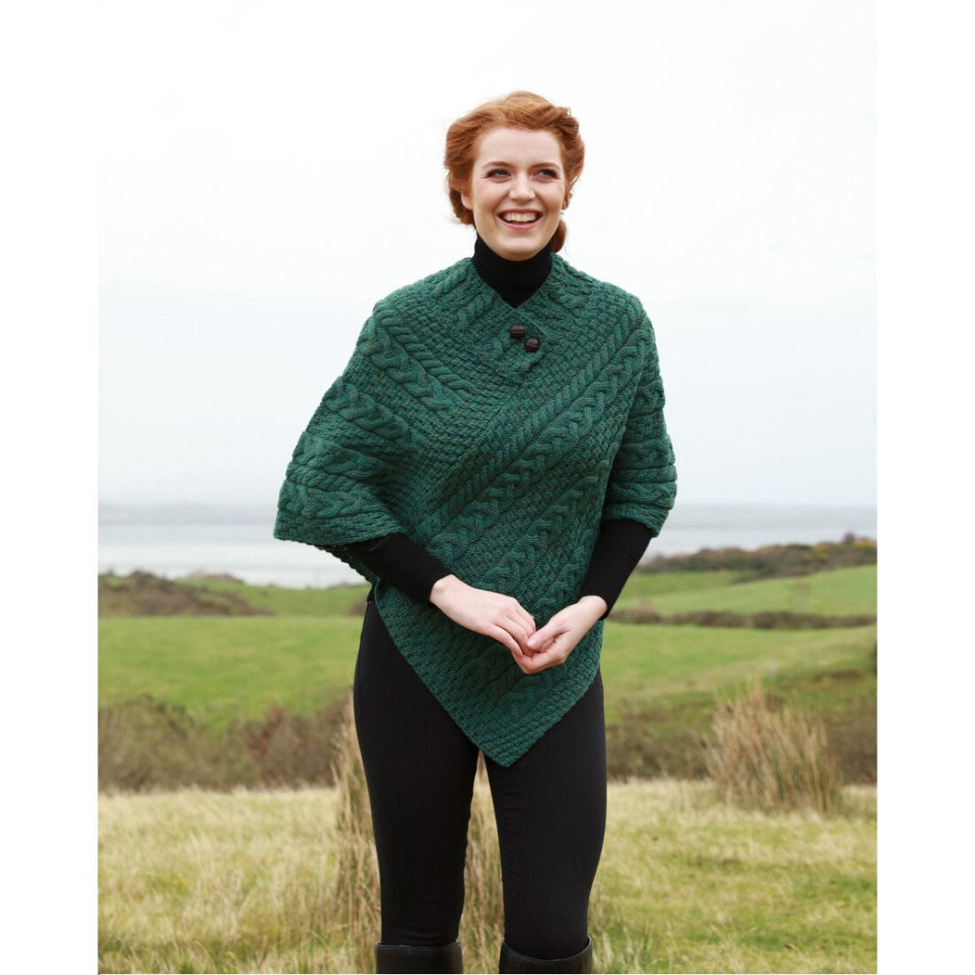 Smiling woman wearing green knitted poncho standing outdoors on grass