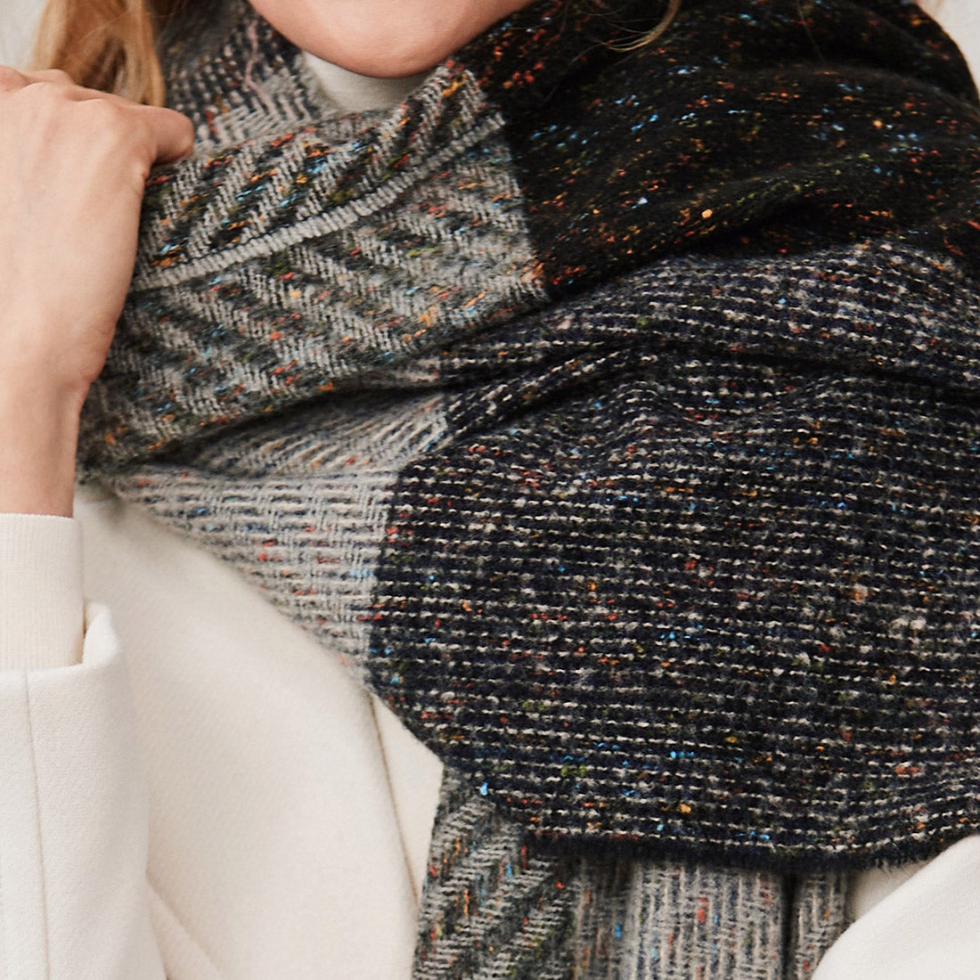 Close-up of person wearing a multicolored textured wool scarf and white coat
