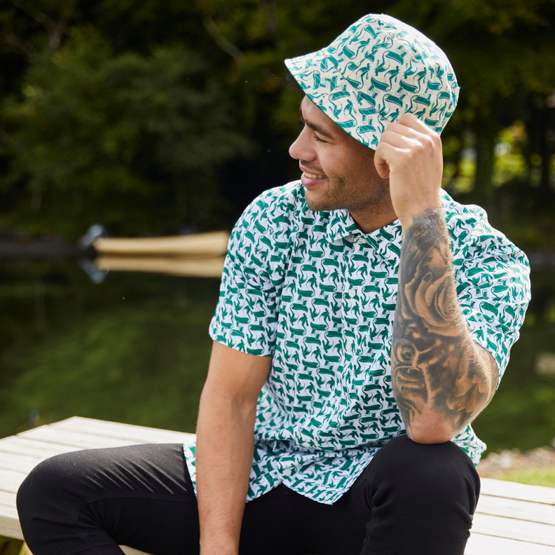 Man sitting outdoors wearing patterned shirt and matching bucket hat, smiling