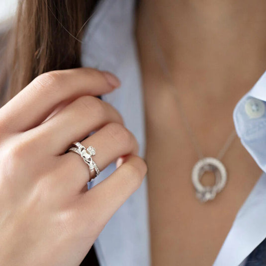 Hand wearing a silver ring with a heart design near a necklace on chest