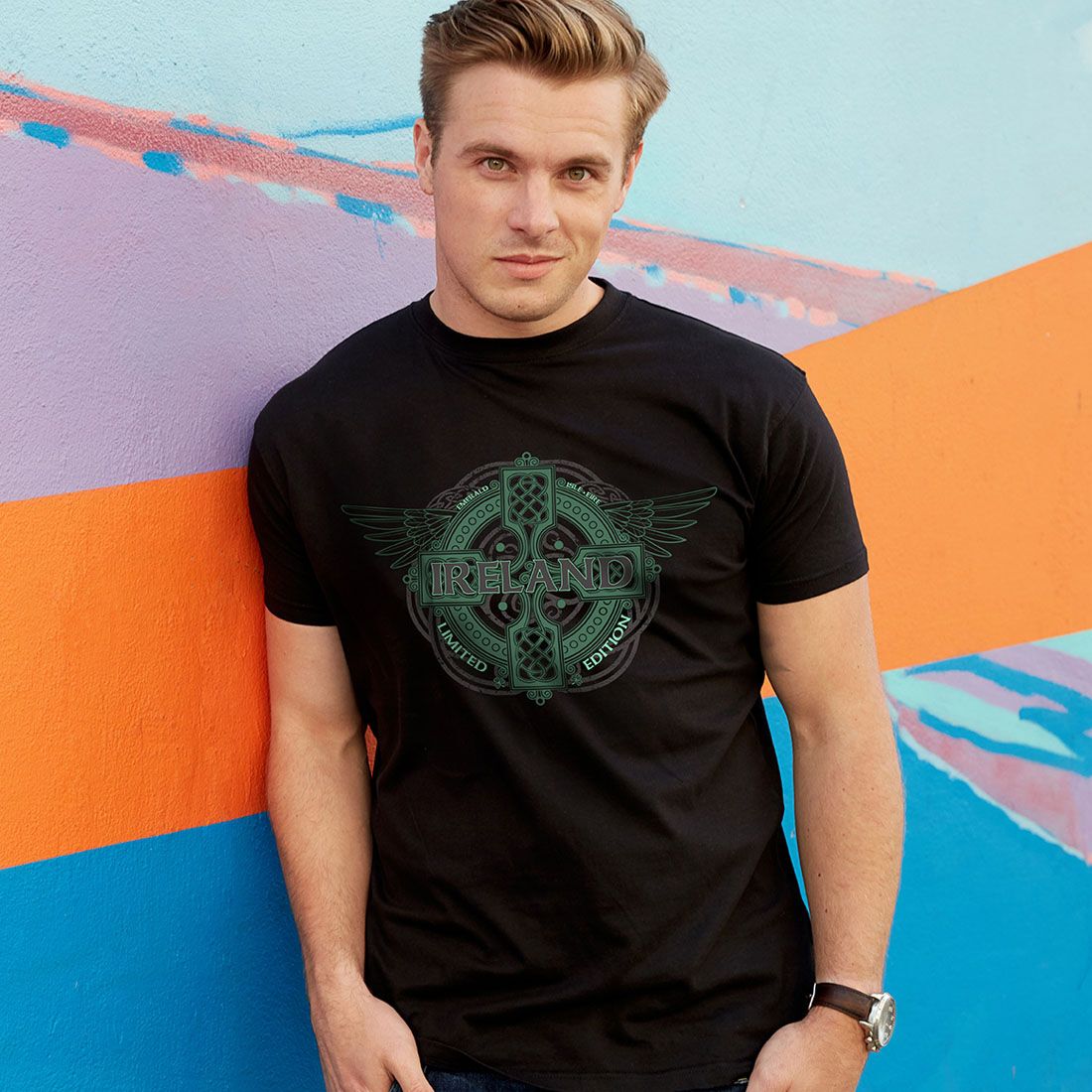 Young man wearing black Ireland graphic t-shirt standing against colorful wall