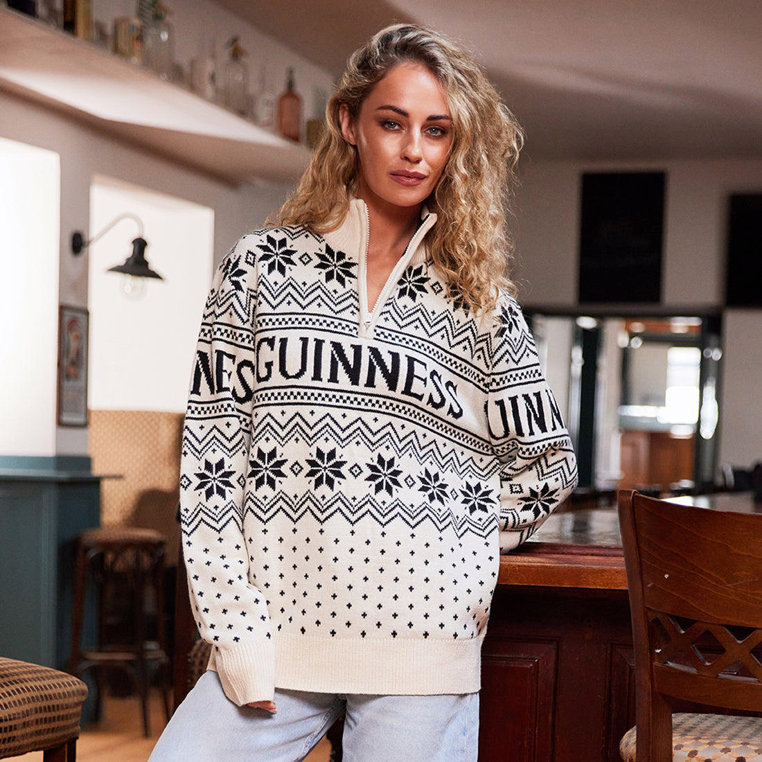 Woman with curly hair wearing a patterned sweater standing indoors